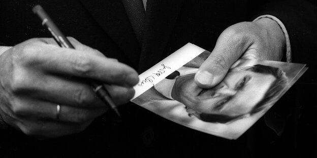 Zwei Hände halten einen Stift und eine Autogrammkarte von Gerhard Schröder Zwei Hände halten einen Stift und eine Autogrammkarte von Gerhard Schröder