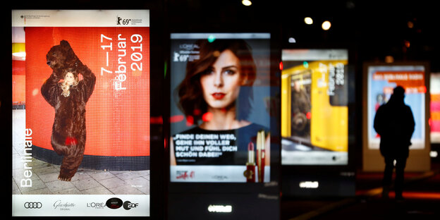 Beleuchtete Werbetafeln säumen einen Bürgersteig in Berlin, ganz vorne das aktuelle Plakat zur Berlinale Beleuchtete Werbetafeln säumen einen Bürgersteig in Berlin, ganz vorne das aktuelle Plakat zur Berlinale