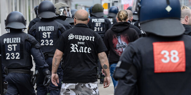 In Halle läuft ein Mann mit einem rassistischen Spruch auf dem Hemd zwischen Polizisten In Halle läuft ein Mann mit einem rassistischen Spruch auf dem Hemd zwischen Polizisten