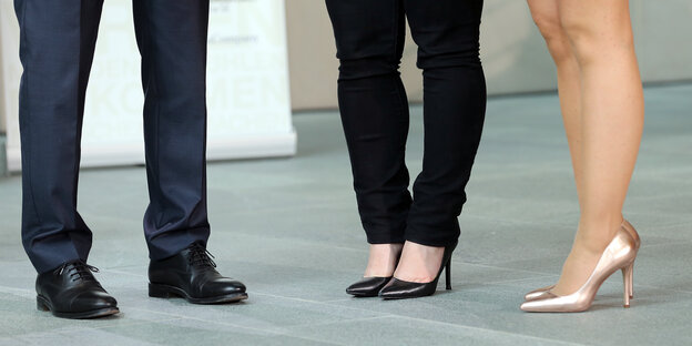 Drei Beinpaare, zwei mit Stöckeln, eins mit Herrenschuhen bekleidet Drei Beinpaare, zwei mit Stöckeln, eins mit Herrenschuhen bekleidet