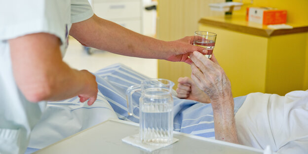 Eine Krankenpflegerin reicht einem Patienten ein Glas Wasser. Eine Krankenpflegerin reicht einem Patienten ein Glas Wasser.