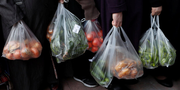 Menschen stehen in einer Schlange und halten Plastiktüten voll mit Gemüse Menschen stehen in einer Schlange und halten Plastiktüten voll mit Gemüse