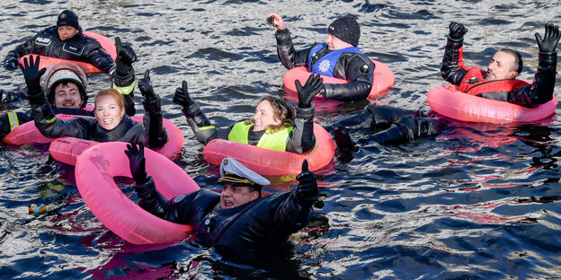 Ein Polizist und weitere Mitarbeiter im öffentlichen Dienst schwimmen mit Rettungsringen in der Hamburger Binnenalster