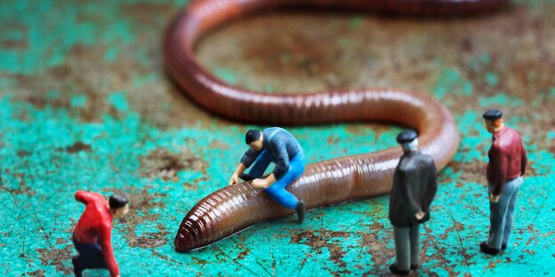 Vor einem Regenwurm stehen Miniatur-Spielfiguren Vor einem Regenwurm stehen Miniatur-Spielfiguren