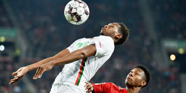 Zwei Fußballer,Augsburgs Reece Joel Oxford (l.) und David Alaba (Bayern München), springen zum Kopfballduell hoch Zwei Fußballer,Augsburgs Reece Joel Oxford (l.) und David Alaba (Bayern München), springen zum Kopfballduell hoch