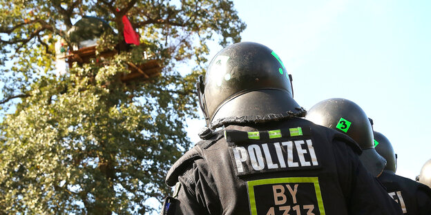 Zwei behelmte Polizisten von hinten, sie schauen zu einem Haus in den Bäumen hovh Zwei behelmte Polizisten von hinten, sie schauen zu einem Haus in den Bäumen hovh