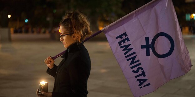 Eine Frau hat eine Kerze und eine lilafarbene Flagge mit dem Schriftzug "Feminista" in der Hand Eine Frau hat eine Kerze und eine lilafarbene Flagge mit dem Schriftzug "Feminista" in der Hand