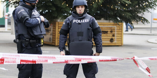 Zwei Polizisten stehen in Schutzkleidung hinter einem Flatterband auf einem Weihnachtsmarkt Zwei Polizisten stehen in Schutzkleidung hinter einem Flatterband auf einem Weihnachtsmarkt