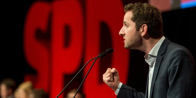 Leohn Hahn, Landeschef der Jungsozialisten Baden-Württemberg, steht auf einer Bühne vor einem Mikrophon und ballt die Faust. Im Hintergrund ist der Schriftzug SPD zu sehen