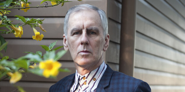 Porträtaufnahme von Robert Forster vor einer Hütte, neben ihm gelbe Blumen Porträtaufnahme von Robert Forster vor einer Hütte, neben ihm gelbe Blumen