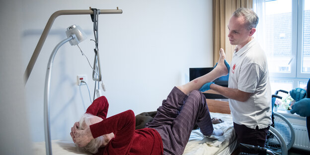 Alte Frau im Bett, Mann untersucht ihr Bein Alte Frau im Bett, Mann untersucht ihr Bein