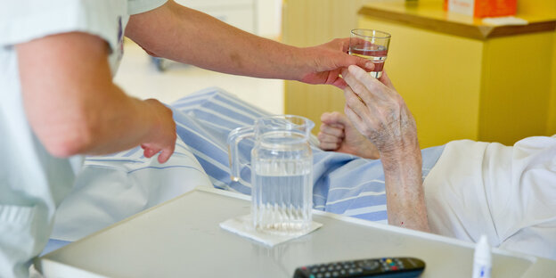 Eine Pflegerin gibt einer im Krankenbett liegenden Person Medizin Eine Pflegerin gibt einer im Krankenbett liegenden Person Medizin