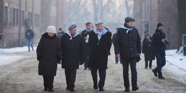 Alte Männer und Frauen mit Häftlingsmützen gehen über das Auschwitz-Gelände. Alte Männer und Frauen mit Häftlingsmützen gehen über das Auschwitz-Gelände.