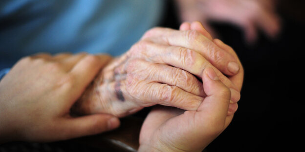 Zwei Hände halten die Hand einer älteren Person Zwei Hände halten die Hand einer älteren Person