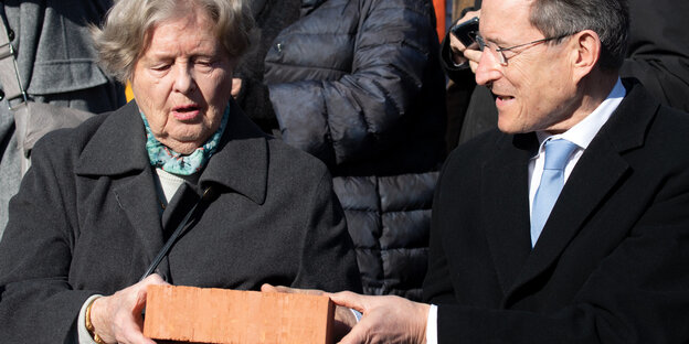 Eine Frau, Marianne von Weizsäcker, und ein Mann, Wolfgang Huber, halten auf der Baustelle der Garnisonkirche in Potsdam einen Ziegelstein