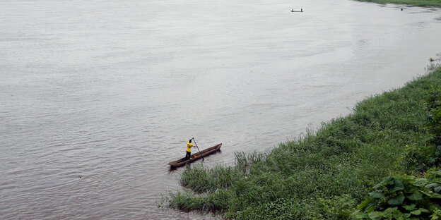 Blick auf den Kongo-Fluss. Ein Mann rudert sein Boot darüber Blick auf den Kongo-Fluss. Ein Mann rudert sein Boot darüber