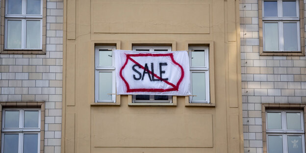 Aus dem Fenster einer Wohnung hängt ein Banner mit der Aufschrift "Sale". Das Wort ist durchgestrichen Aus dem Fenster einer Wohnung hängt ein Banner mit der Aufschrift "Sale". Das Wort ist durchgestrichen