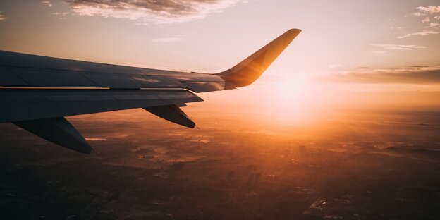 Die Tragfläche eines Flugzeugs, dahinter die aufgehende Sonne Die Tragfläche eines Flugzeugs, dahinter die aufgehende Sonne