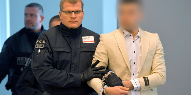 Ein Polizist führt den Angeklagten Alaa S. in Handschellen in den Gerichtsaal. Gesicht des Angeklagte ist verpixelt Ein Polizist führt den Angeklagten Alaa S. in Handschellen in den Gerichtsaal. Gesicht des Angeklagte ist verpixelt