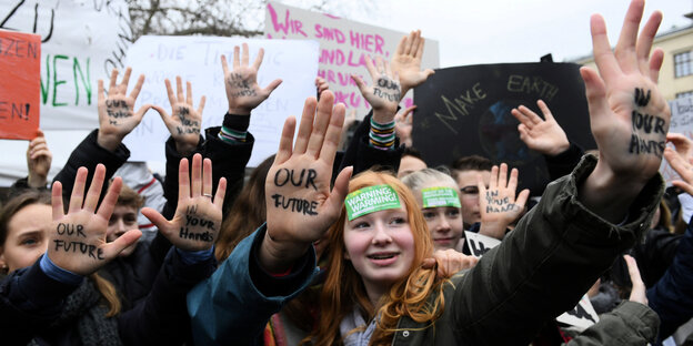 Jugendlich auf einer Klimademo, sie strecken die Innenhand nach vorn, auf ihnen steht: "Our Future" und "In your hands" Jugendlich auf einer Klimademo, sie strecken die Innenhand nach vorn, auf ihnen steht: "Our Future" und "In your hands"