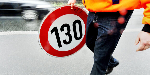 Eine Person trägt ein Verkehrsschild, das 130 km pro Stunde als Höchstgeschwindigkeit vorschreibt Eine Person trägt ein Verkehrsschild, das 130 km pro Stunde als Höchstgeschwindigkeit vorschreibt