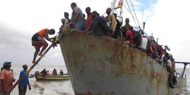 Menschen steigen von einem verrosteten Boot an Land Menschen steigen von einem verrosteten Boot an Land