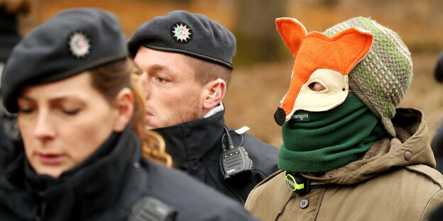 Eine Person mit Fuchsmaske zwischen Polizisten Eine Person mit Fuchsmaske zwischen Polizisten