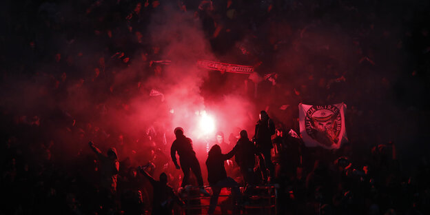 Eine Menschenmenge beim Fußball. Es ist dunkel, jemand hat ein bengalisches Feuer entzündet