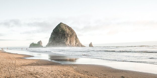 Ein Felsen im Meer vor einem Sandstrand