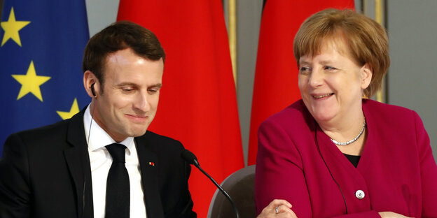 Macron und Merkel sitzen nebeneinander Macron und Merkel sitzen nebeneinander