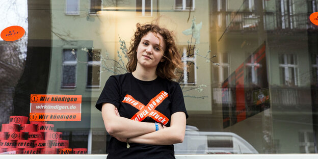 Junge Frau steht vor einem Schaufenster. Auf ihrem T-Shirt steht "unfuck the world" Junge Frau steht vor einem Schaufenster. Auf ihrem T-Shirt steht "unfuck the world"