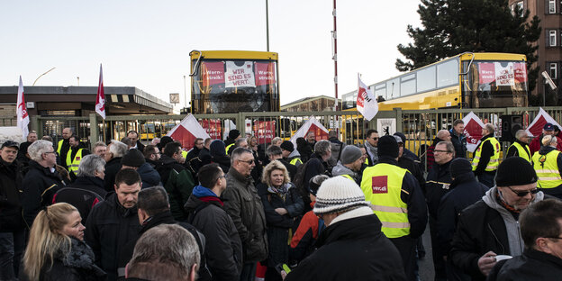 Menschen vor einer vergitterten Einfahrt, in der zwei Busse stehen Menschen vor einer vergitterten Einfahrt, in der zwei Busse stehen
