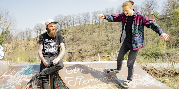 Tobias Burdukats sitzt auf einer Halfpipe, ein junger Mann fährt dort mit seinem Skateboard Tobias Burdukats sitzt auf einer Halfpipe, ein junger Mann fährt dort mit seinem Skateboard