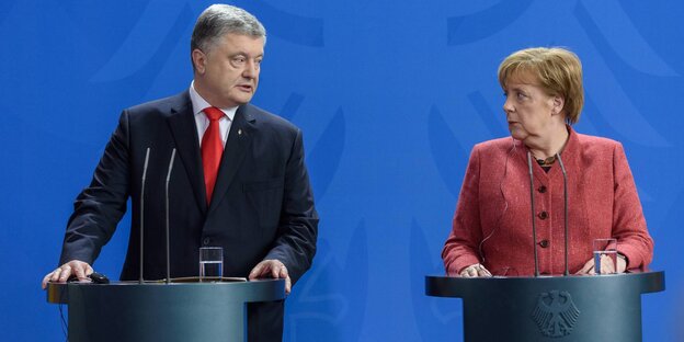 Petro Poroschenko und Angela Merkel stehen an Rednerpulten und gucken sich gerade an. Petro Poroschenko und Angela Merkel stehen an Rednerpulten und gucken sich gerade an.