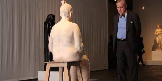 Ein Mann im Anzug betrachtet eine weiße Skulptur einer Mutter Ein Mann im Anzug betrachtet eine weiße Skulptur einer Mutter