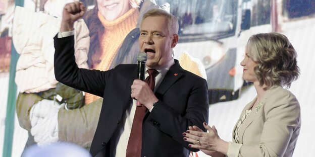 Ein Mann hält ein Mikro in der linken Hand und streckt die andere Faust nach oben. Neben ihm steht eine Frau und klatscht in die Hände. Ein Mann hält ein Mikro in der linken Hand und streckt die andere Faust nach oben. Neben ihm steht eine Frau und klatscht in die Hände.