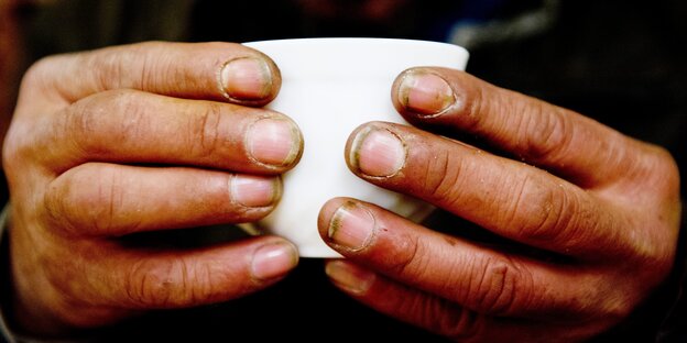 Ein obdachloser Mann hält in einem Nachtcafé eine Tasse. Ein obdachloser Mann hält in einem Nachtcafé eine Tasse.