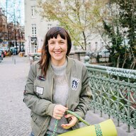 Eine Frau steht auf einer Brücke, hält eine Yogamatte in der Hand und lacht Eine Frau steht auf einer Brücke, hält eine Yogamatte in der Hand und lacht