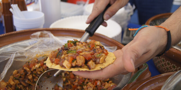 Ein Taco liegt auf einer Hand, es wird gerade gefüllt Ein Taco liegt auf einer Hand, es wird gerade gefüllt