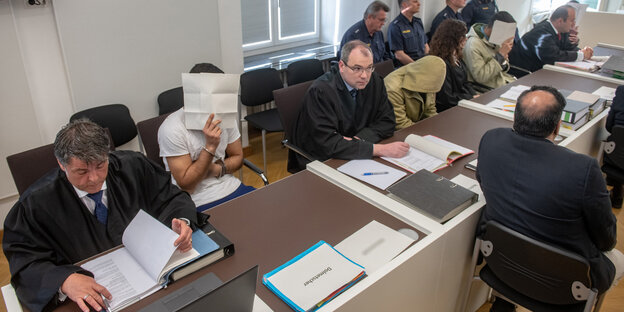 Menschen sitzen an einem langen Tisch, auf dem Akten liegen