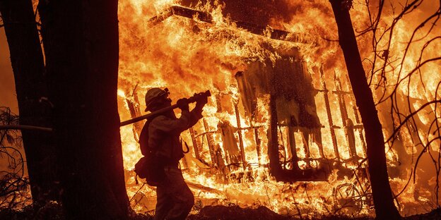 Ein feuerwehrmann trägt einen Löschschlauch zu einem brennenden Haus Ein feuerwehrmann trägt einen Löschschlauch zu einem brennenden Haus