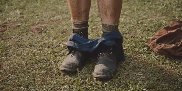 Männliche Beine in Arbeitsschuhen, auf denen eine heruntergelassene Unterhose liegt, daneben im Gras liegt ein T-Shirt. Männliche Beine in Arbeitsschuhen, auf denen eine heruntergelassene Unterhose liegt, daneben im Gras liegt ein T-Shirt.