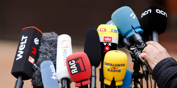 Mikrofone von diversen deutschen und internationalen Medien, davor eine Hand, die ein Mikrofon einrichtet Mikrofone von diversen deutschen und internationalen Medien, davor eine Hand, die ein Mikrofon einrichtet