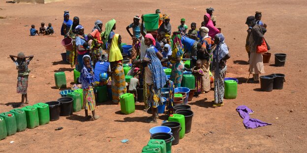 Auf rötlichem Sand Frauen und Kinder sich mit leeren Wasserkanister, grüne und blaue.