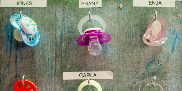 Schnuller hängen an beschrifteten Haken. Ein blauer für "Jonas" und pinke für "Carla" und "Enja" Schnuller hängen an beschrifteten Haken. Ein blauer für "Jonas" und pinke für "Carla" und "Enja"