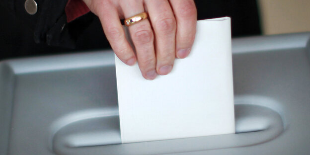 Hand wirft Umschlag in eine Wahlurne Hand wirft Umschlag in eine Wahlurne