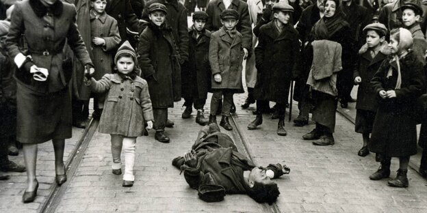 Schwarz-weiß-Foto: Ein Mann liegt auf der Straße, Kinder stehen um ihn herum Schwarz-weiß-Foto: Ein Mann liegt auf der Straße, Kinder stehen um ihn herum