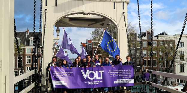 Eine Gruppe von Menschen halten ein lila Transparent auf einer Brücke Eine Gruppe von Menschen halten ein lila Transparent auf einer Brücke