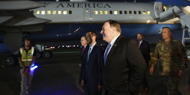 Pompeo läuft im Dunkeln am Flughafen, hinter ihm Leute und ein Flugzeug Pompeo läuft im Dunkeln am Flughafen, hinter ihm Leute und ein Flugzeug