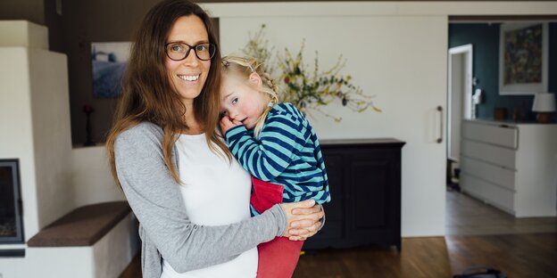 Eine Frau mit dunklen langen Haaren hat ein etwa vierjähriges Mädchen auf dem Arm